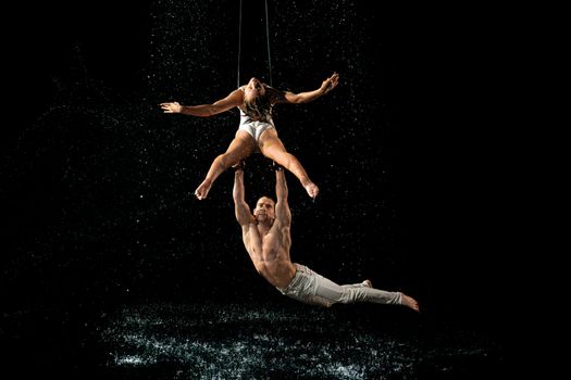 A mesmerizing duo performs aerial acrobatics amidst splashing water on a dark stage.