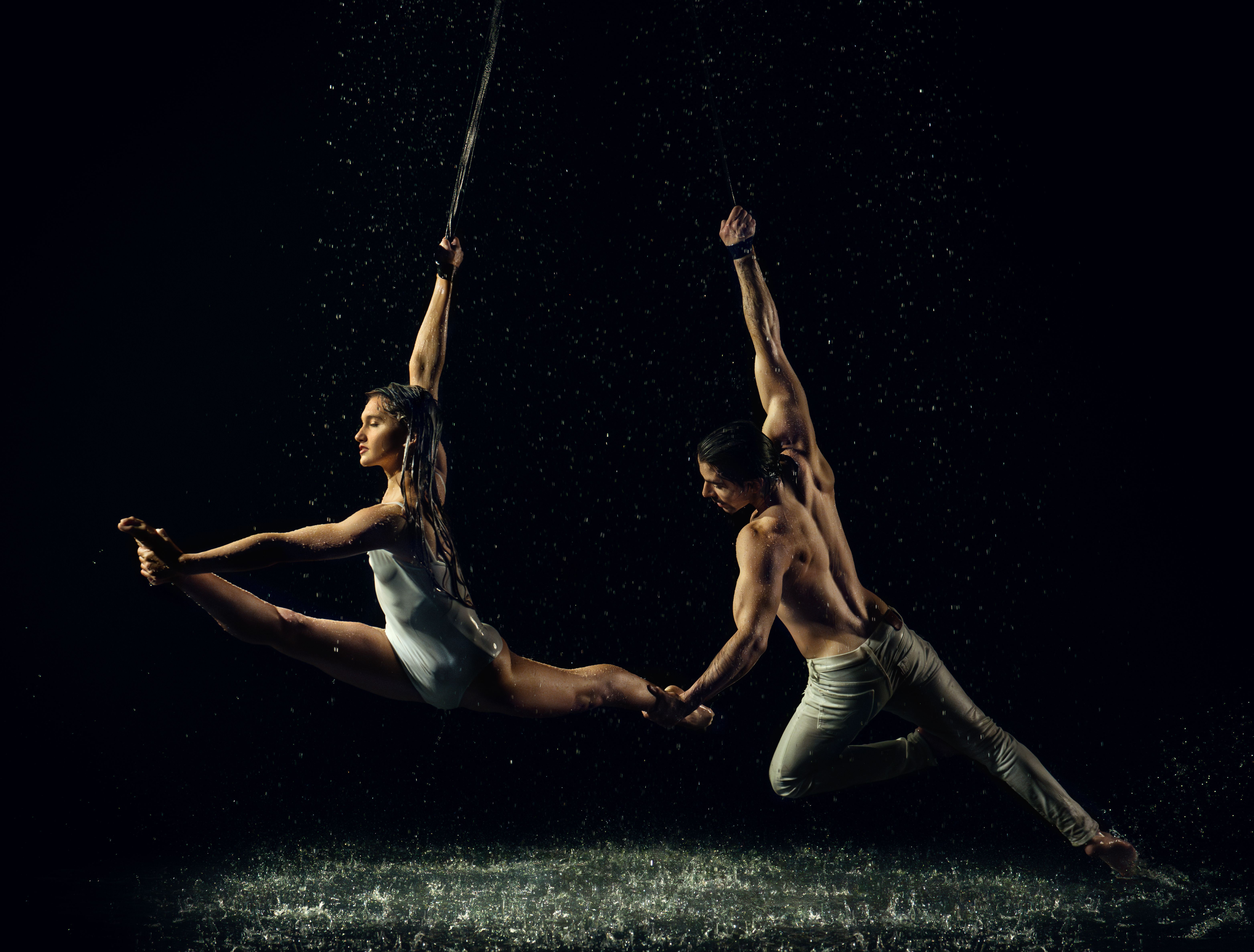 A captivating scene of two dancers performing an aerial routine amidst cascading water.