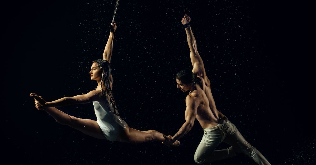 A captivating scene of two dancers performing an aerial routine amidst cascading water.