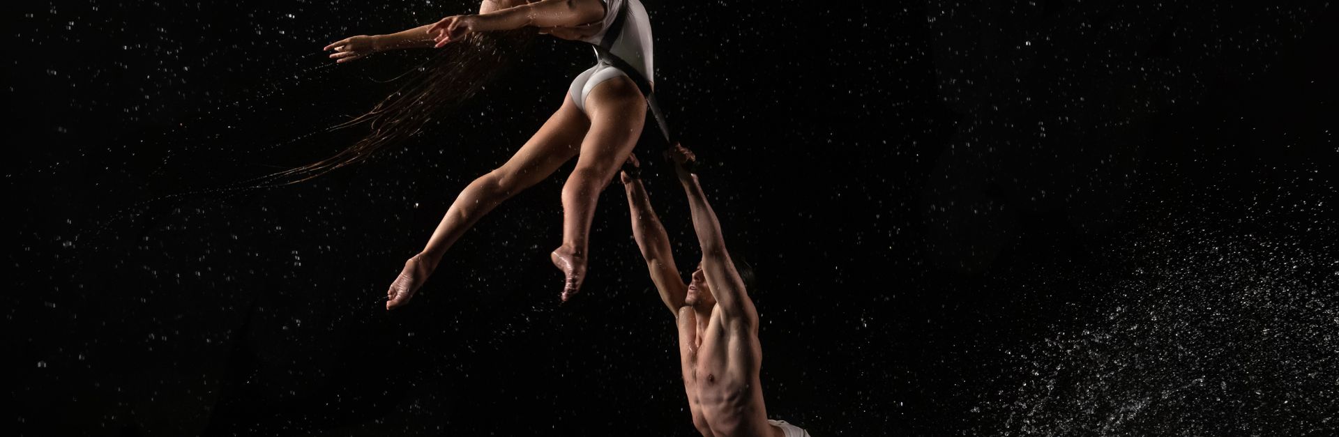 Captivating aerial dance with dynamic water splashes against a dark background.