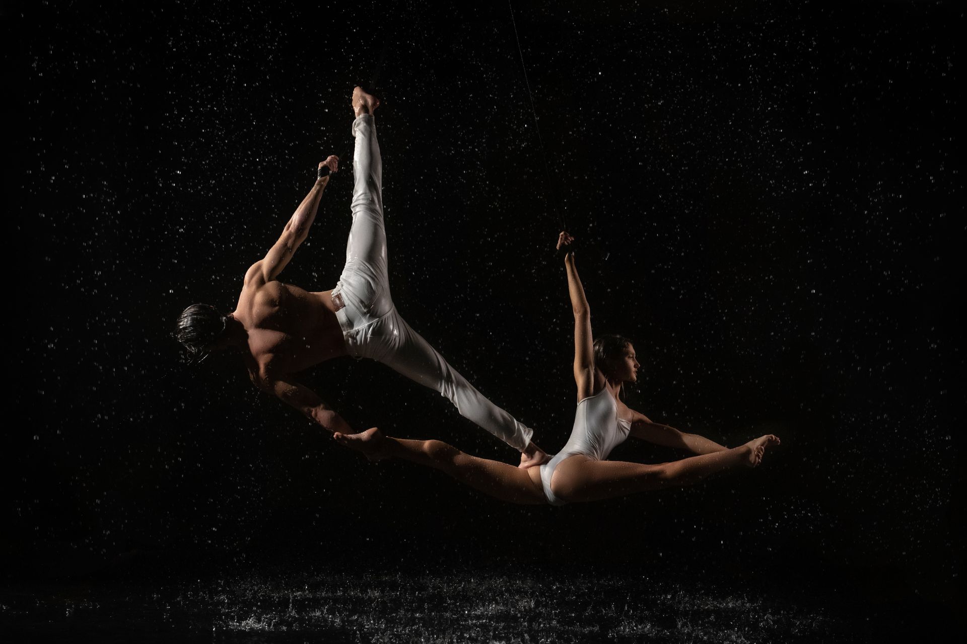 Two athletes perform an acrobatic dance in mid-air against a black backdrop, showcasing strength and
