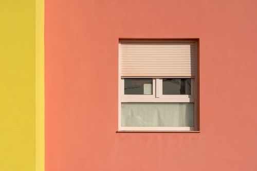 Free A minimalist photo of a pink and yellow building facade with a closed window, emphasizing color contrasts and clean lines. Stock Photo