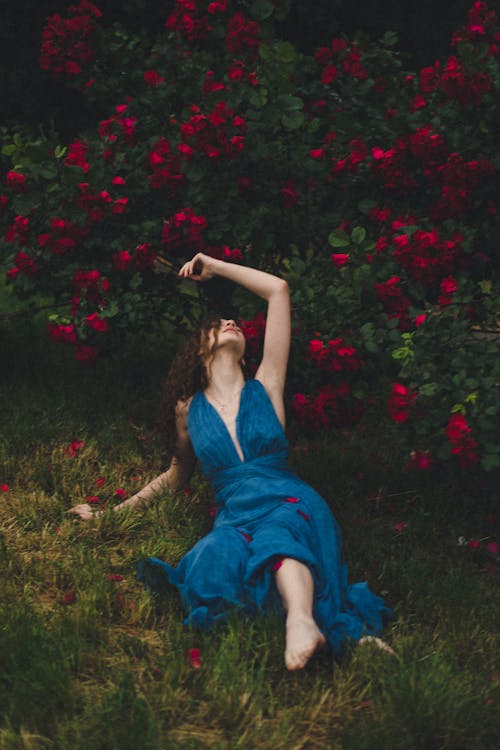 Woman in a Blue Dress Lying under a Flower Shrub 