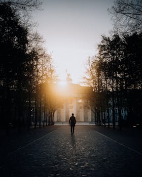 A man walks through Berlin's iconic Brandenburg Gate at sunrise, creating a dramatic silhouette.