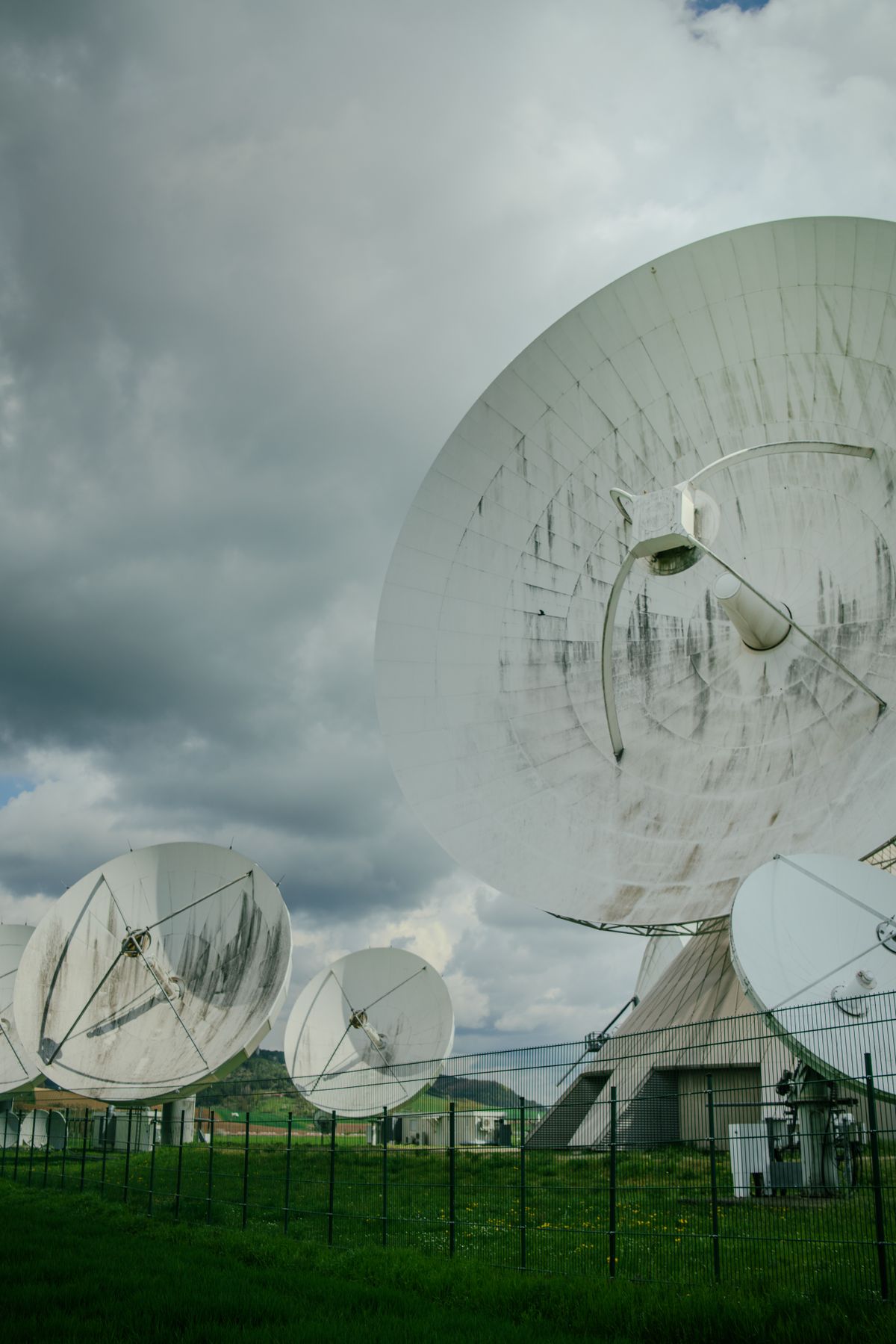 Multiple large satellite dishes at a communication facility under a cloudy sky. Illustrative editorial photograph.