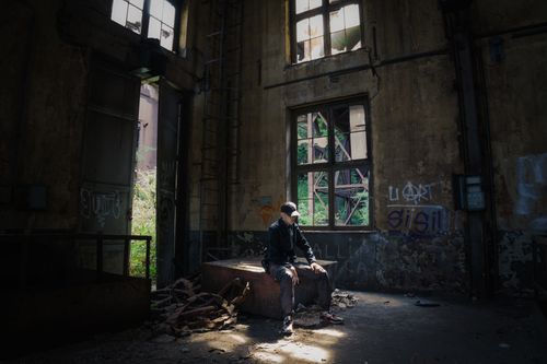 Free A man sits inside an abandoned building with graffiti on the walls, sunlight streaming through broken windows. Stock Photo
