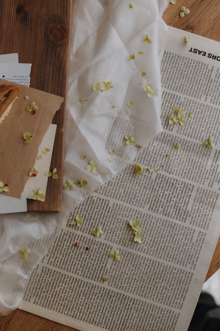 Tiny Petals Scattered On A Newspaper And White Fabric 