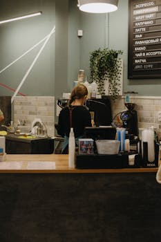 A barista making coffee in a contemporary café setting with a stylish interior and a menu on the wall.
