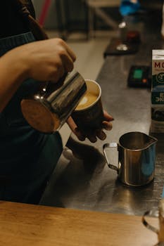 Close-up of a barista pouring milk to create latte art in a café setting. Warm ambiance.