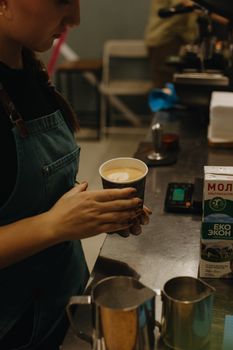 Barista crafting latte art on an espresso in a bustling coffee shop environment.