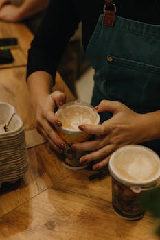 A close-up of a barista serving hot coffee drinks in a cozy cafe setting.