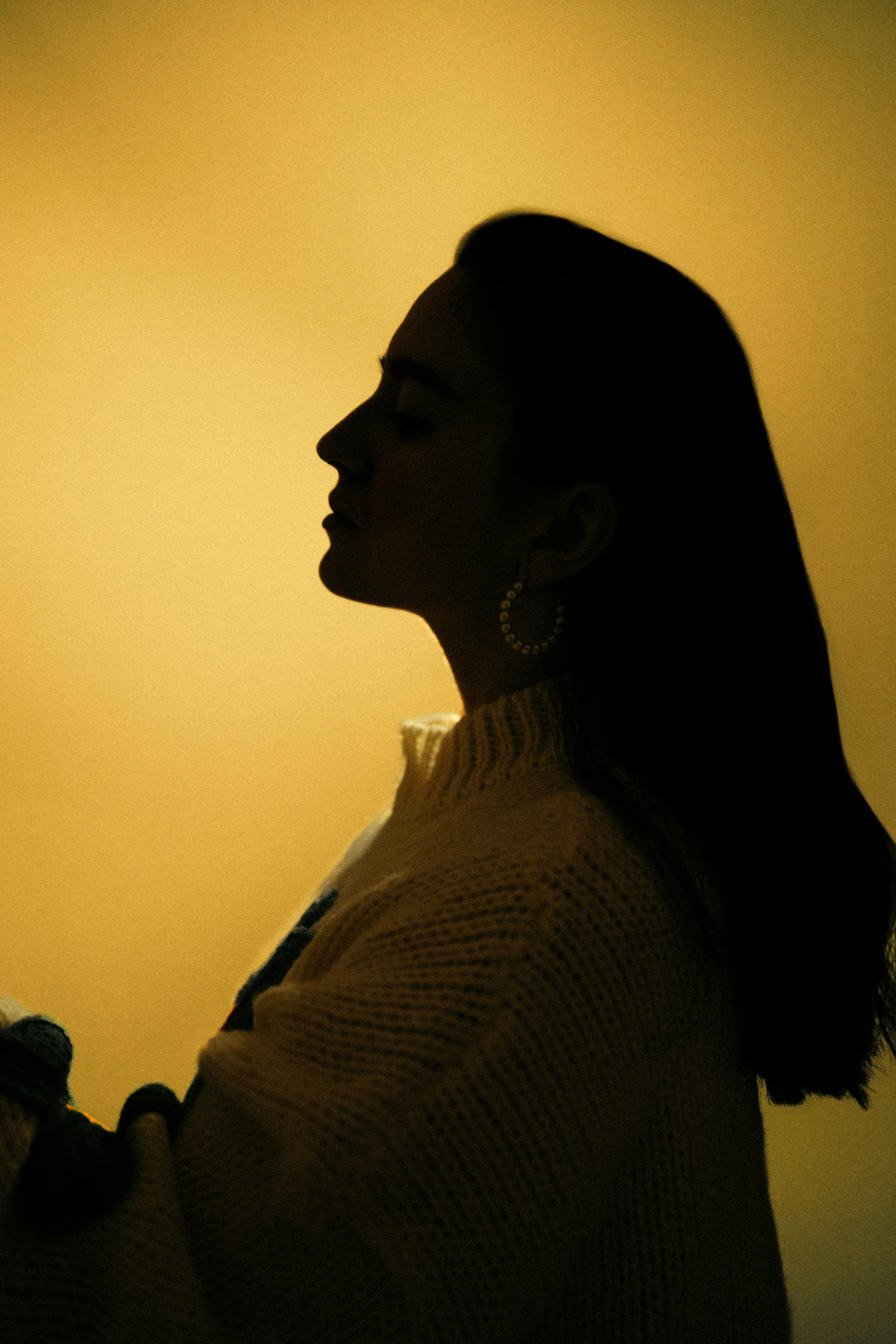Silhouette of a woman in sweater against a warm background, capturing an elegant profile.