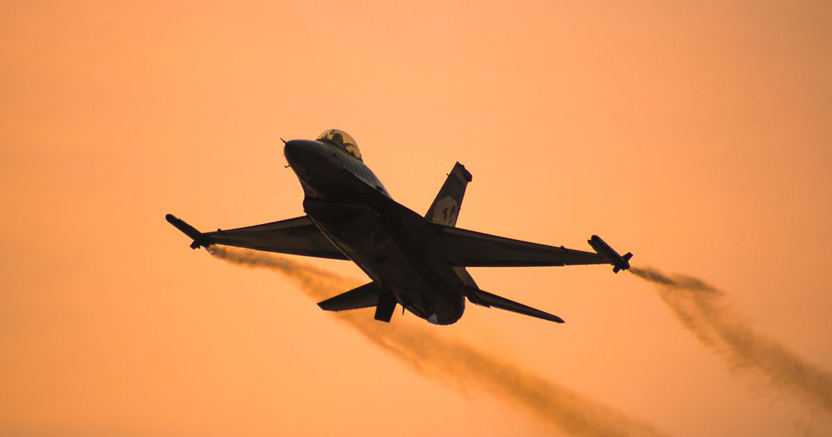 Silhouette of an F-16 fighter jet against a sunset sky.