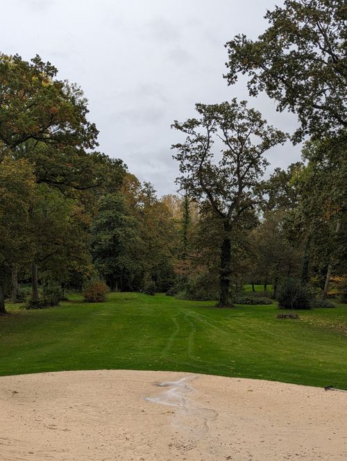 Free A tranquil view of a lush green golf course surrounded by trees and a sand trap in the foreground. Stock Photo