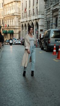 Young woman in fashionable attire walking along an urban city street, showcasing modern style.