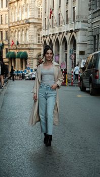 Elegant woman with long black hair walking confidently on a city street during the day.