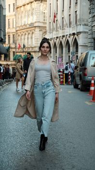 Fashionable woman in trench coat confidently walking on a bustling city street.