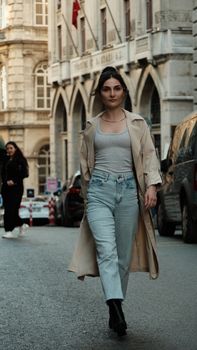 Stylish woman in trench coat walking confidently on city street.