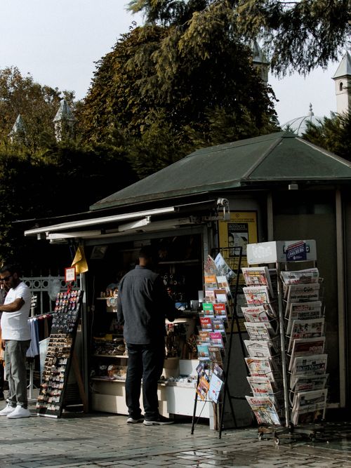 Free A man browsing newspapers and magazines at an outdoor newsstand on a city sidewalk. Stock Photo
