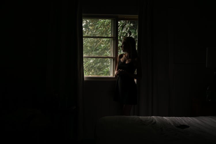 Woman Standing By The Window In A Dark Room 