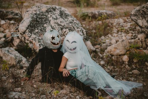 Free Couple with carved pumpkins on heads enjoying a fall-themed photo shoot in rocky outdoors. Stock Photo