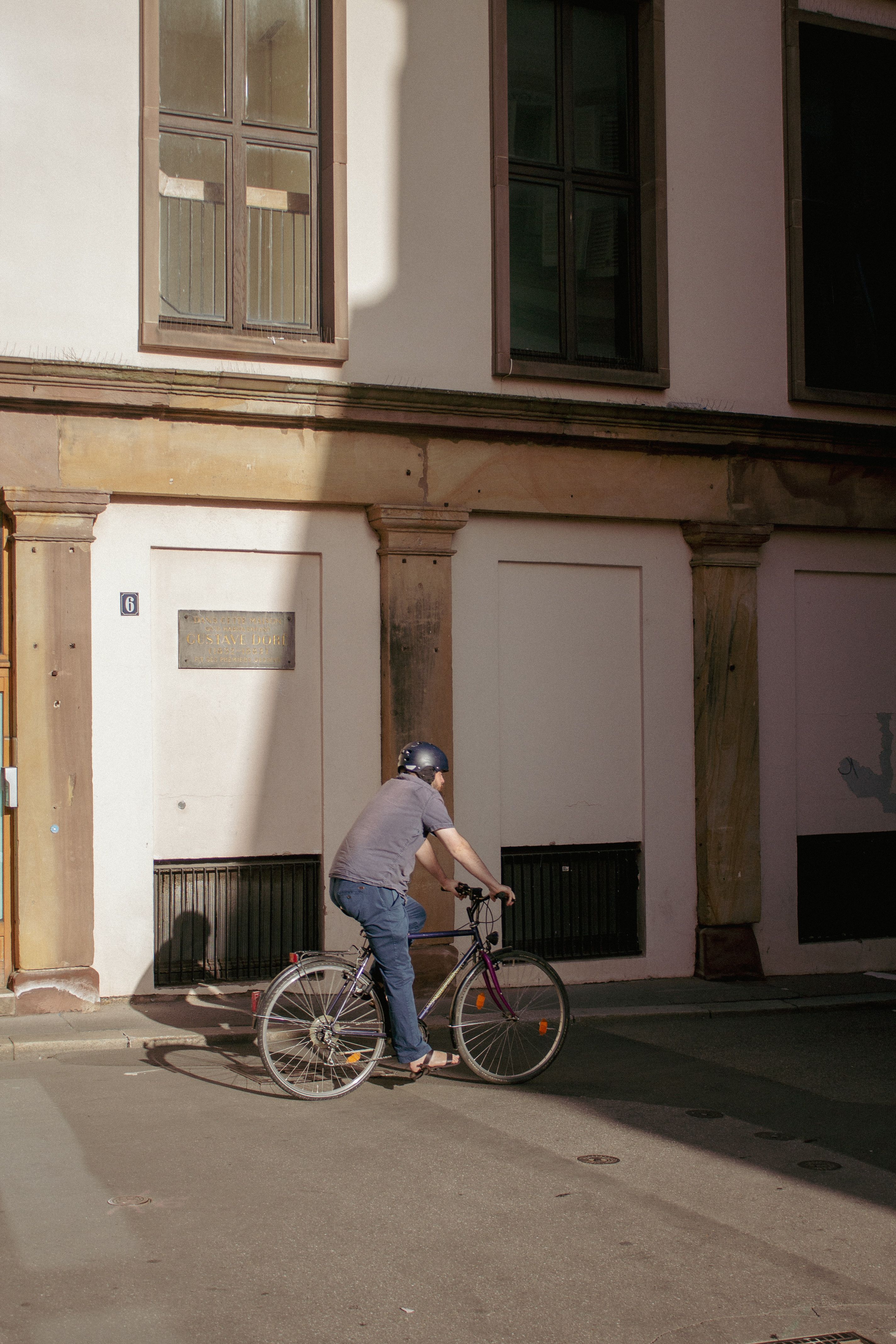 Cycliste circulant dans une rue ensoleillée de Strasbourg bordée d'immeubles bas.