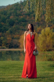 Model in a red dress standing gracefully in a scenic outdoor setting