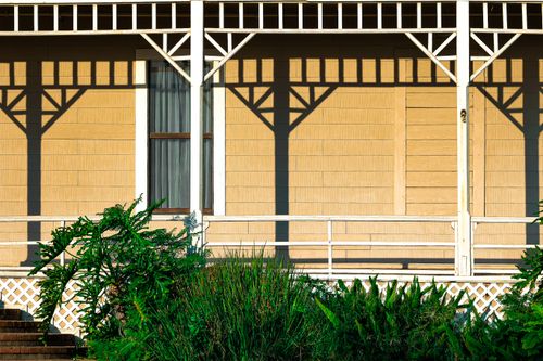 Free Charming wooden house facade with intricate white railings and green plants. Stock Photo