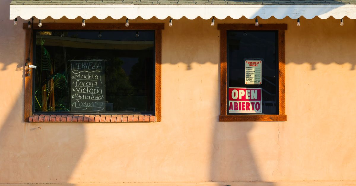 Facade of a local bar with an open sign in English and Spanish under warm sunlight.
