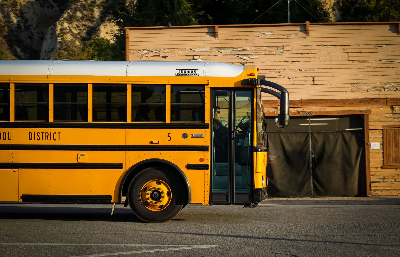 A classic yellow school bus parked on a city street with a rustic wooden building behind it.