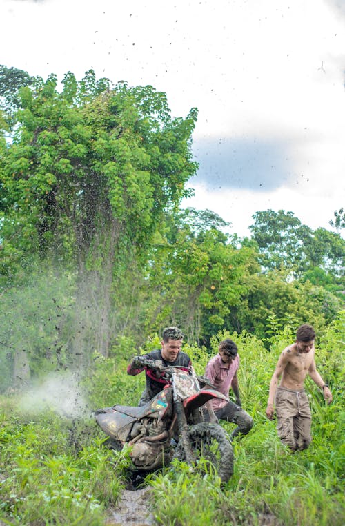 A Man Walking with a Dirt Bike Covered in Mud 