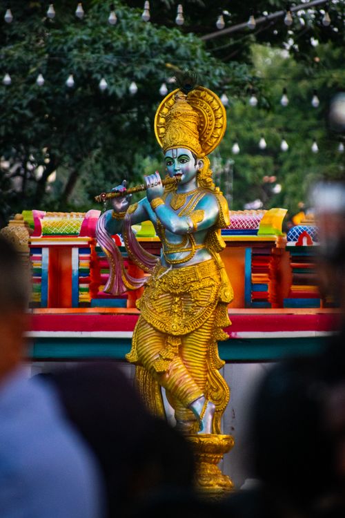 Free Colorful statue of Lord Krishna playing the flute outdoors, surrounded by greenery. Stock Photo