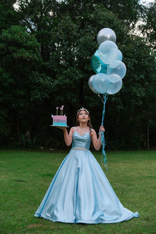 Young Woman Wearing a Princess Dress and a Tiara and Holding Balloons and a Cake