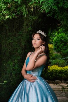 A confident woman in a shimmering blue dress and tiara poses outdoors.