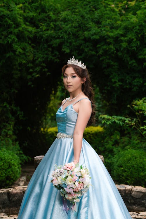 Woman in a Princess Dress Standing in a Garden and Holding a Bouquet of Flowers