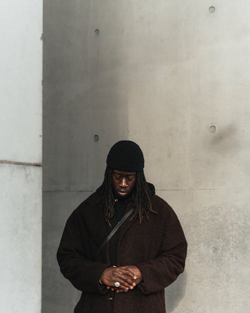 Man in a Brown Coat and a Beanie Standing against the Wall 