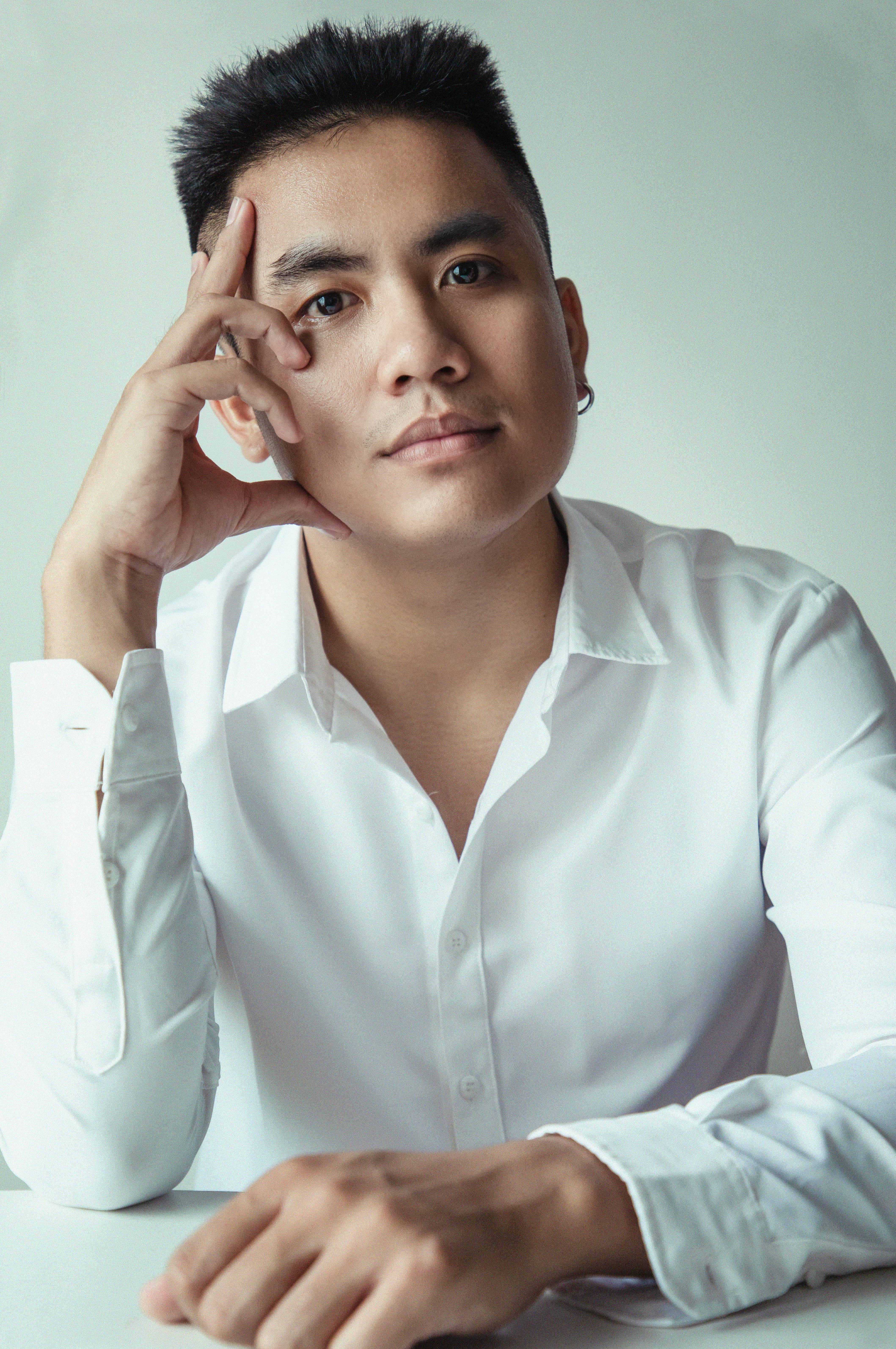 A portrait of a thoughtful man sitting at a table, wearing a white shirt, captured indoors.