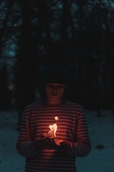 晚上，一个穿着条纹毛衣的人在户外举着小火焰，发出温暖的光芒