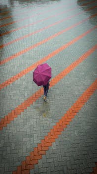 Aerial view of a woman walking with a purple umbrella on a rainy town square.