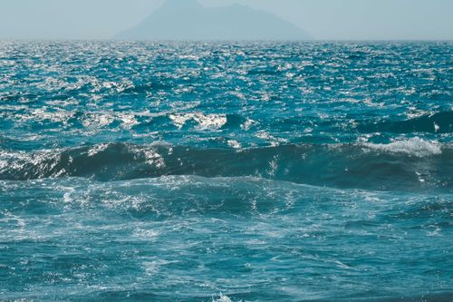 Free Captivating view of blue ocean waves under a bright sky with a distant island. Stock Photo