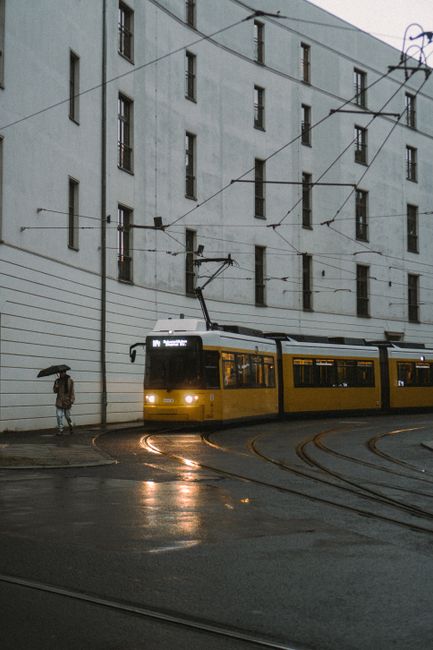 Yellow tram navigating a rainy street in Berlin, showcasing architectural facades and urban transit.