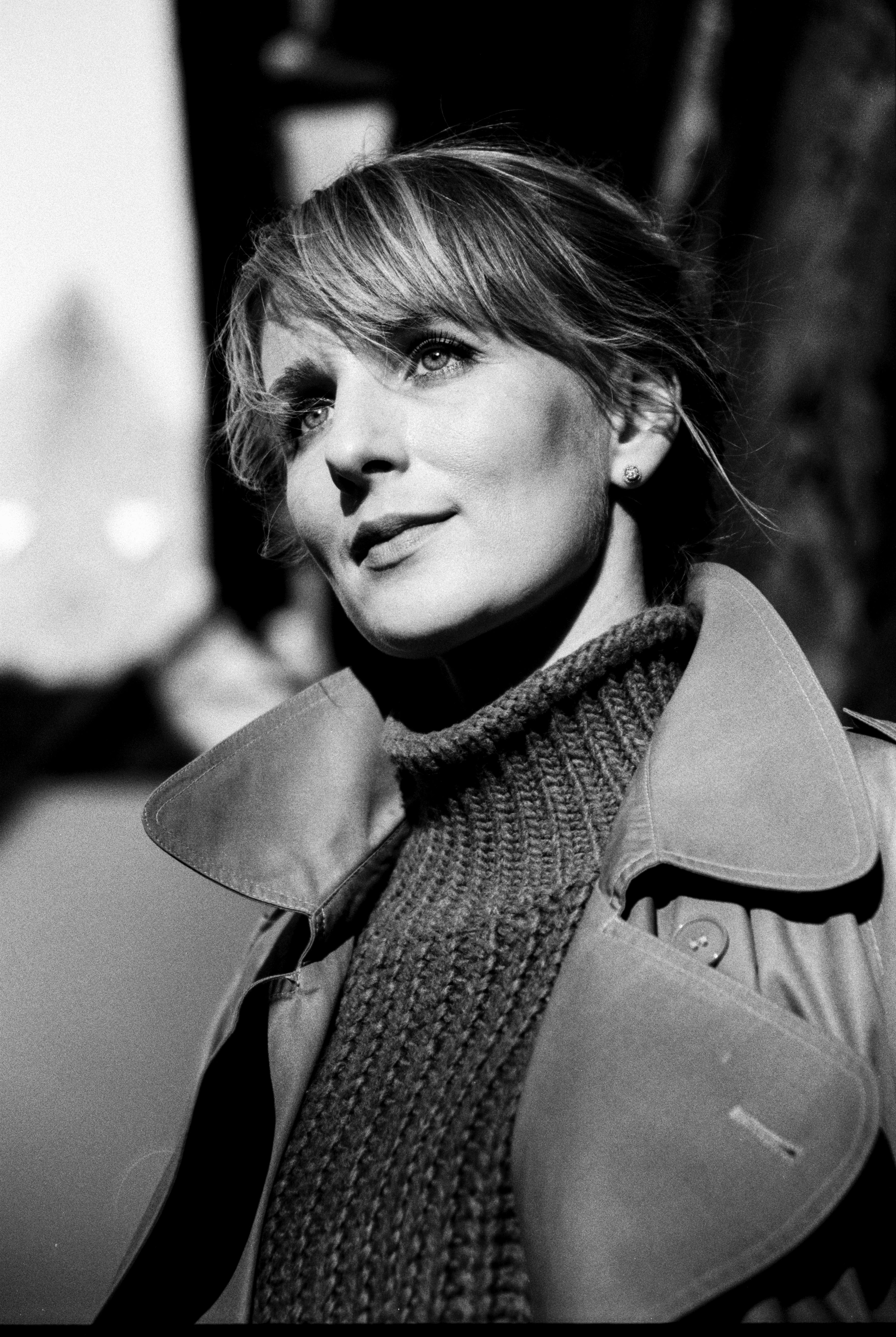 Elegant black and white portrait of a stylish woman in a trench coat, captured in natural light.