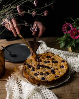 Close-up of a cherry cake being sliced on a rustic wooden table with floral decoration.