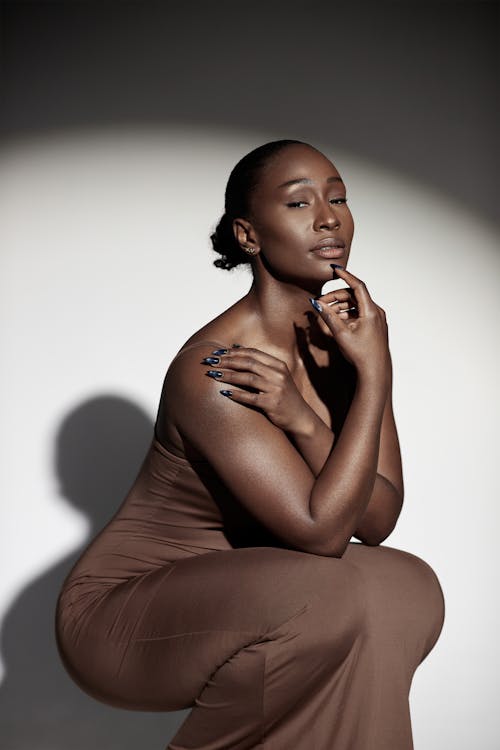 Female Model Wearing a Brown Dress Crouching against a White Background