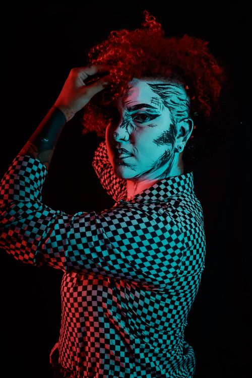 Free Artistic portrait of a model with painted face and curly hair under red and blue lighting. Stock Photo