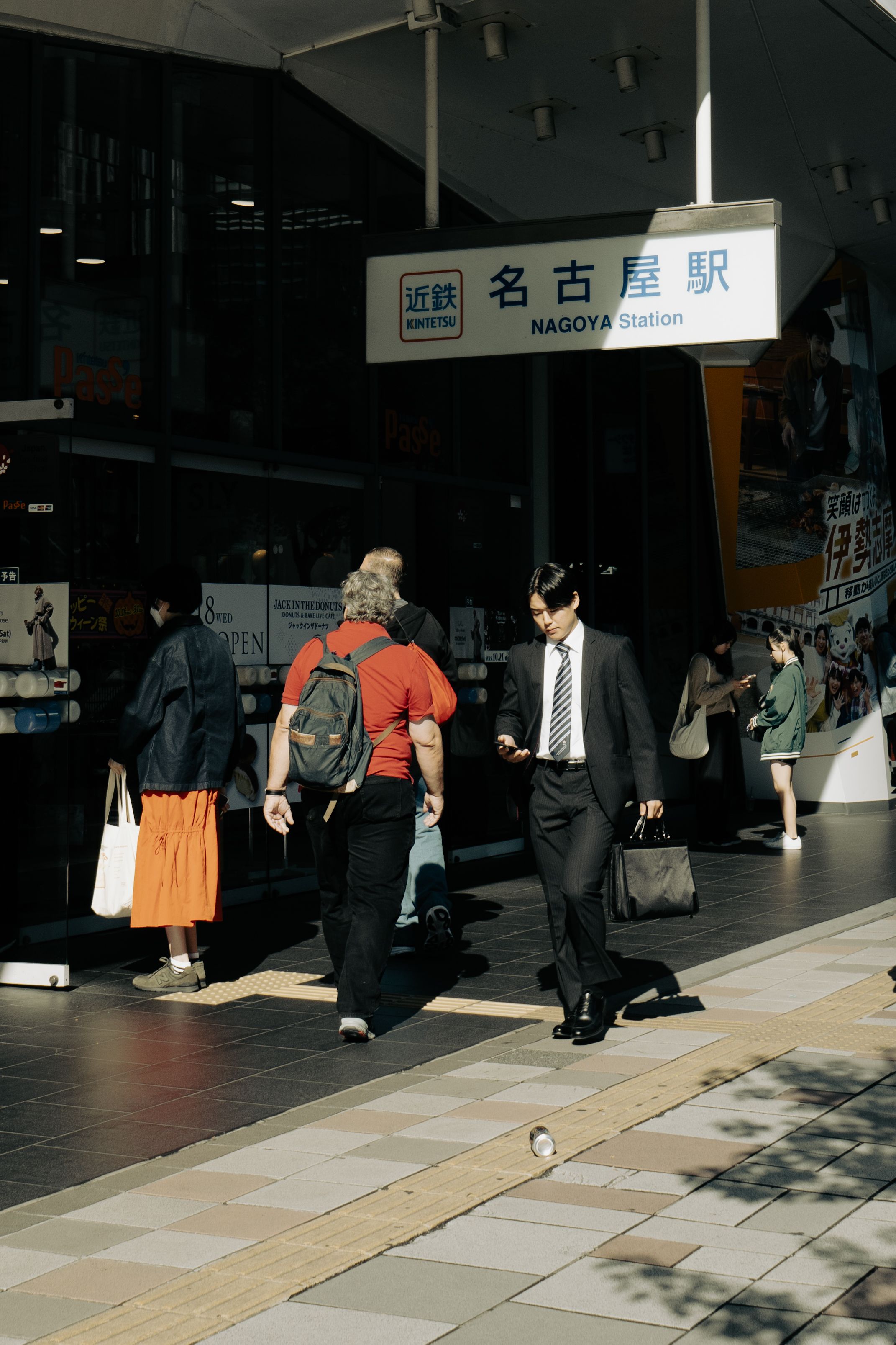 Commuters walking at the entrance of Nagoya Station, Japan, under sunlight.