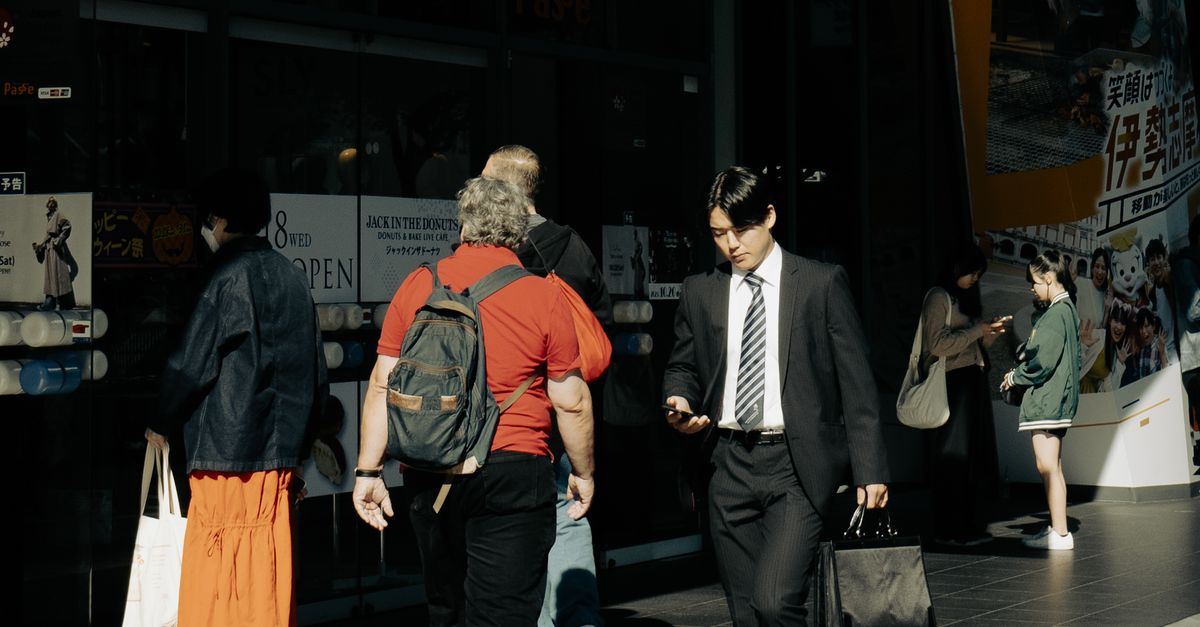 Commuters walking at the entrance of Nagoya Station, Japan, under sunlight.