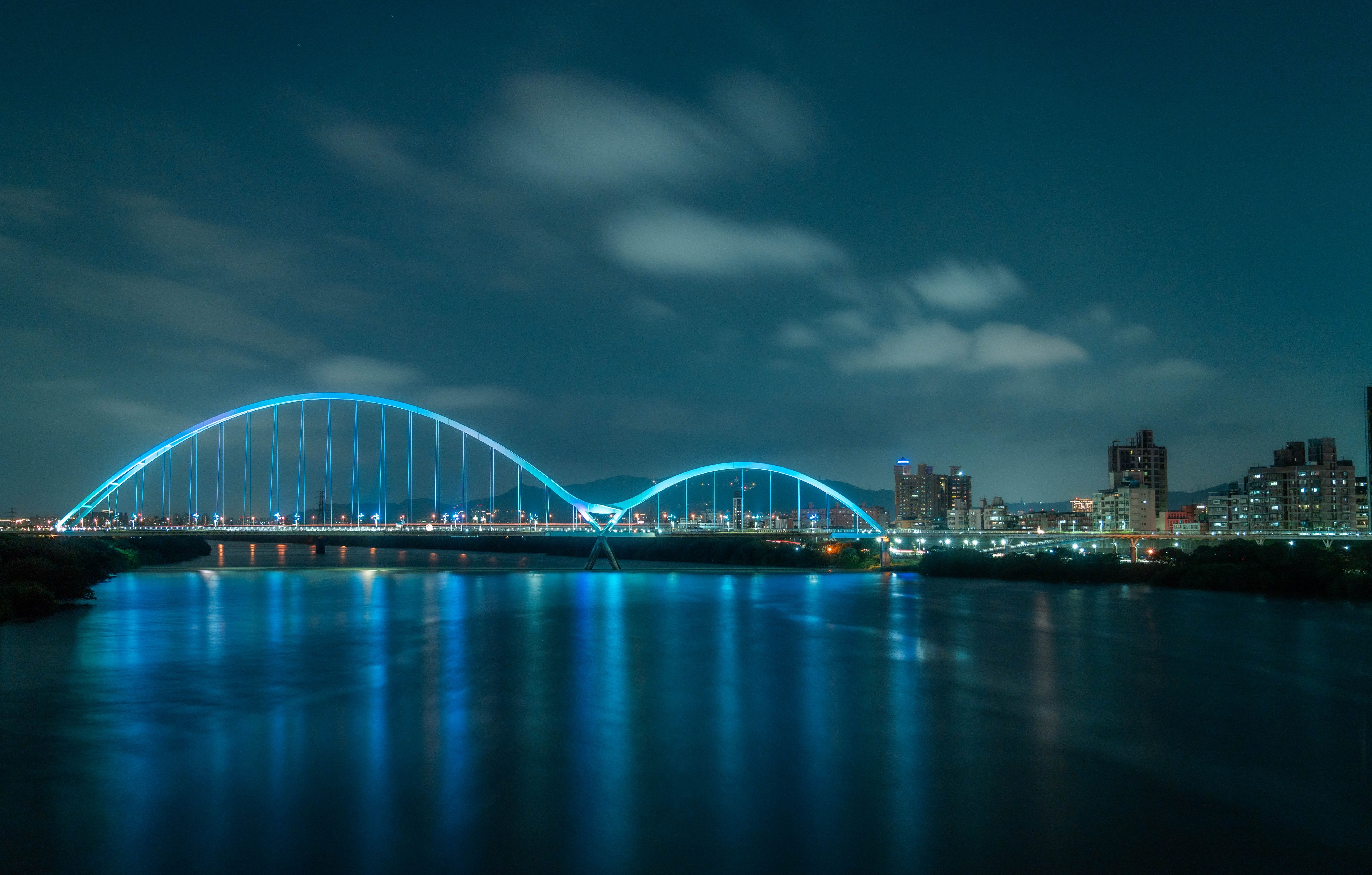 Spectacular illuminated bridge over river in Taipei cityscape at night, showcasing urban beauty.