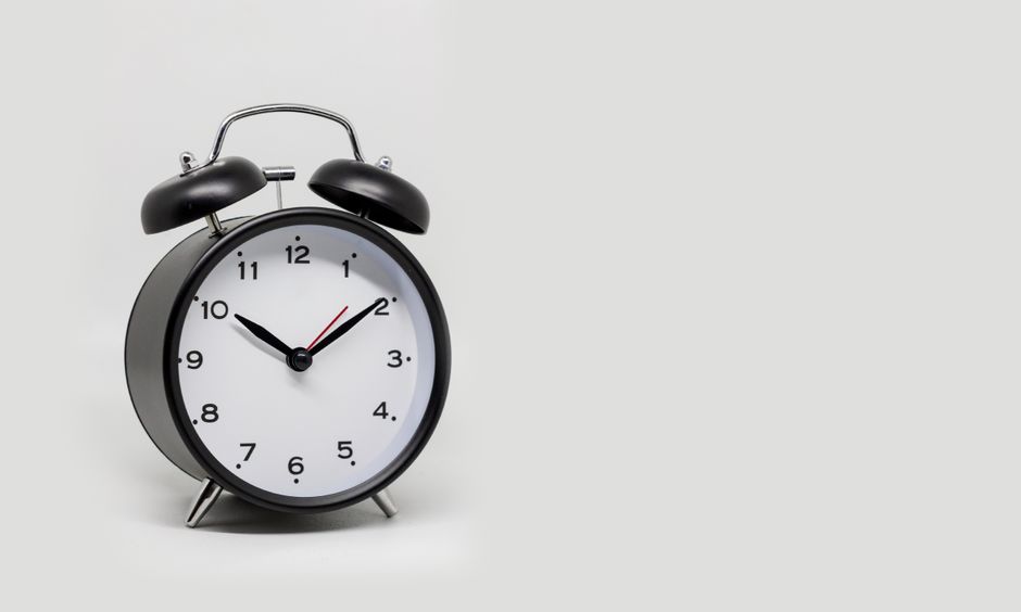 Does a Sunrise Alarm Clock Really Ease Morning Grogginess? Close-up of a classic black alarm clock with a white face on a white background.