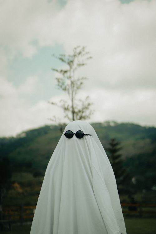 Free A spooky ghost costume with sunglasses standing in a vibrant outdoor setting. Stock Photo